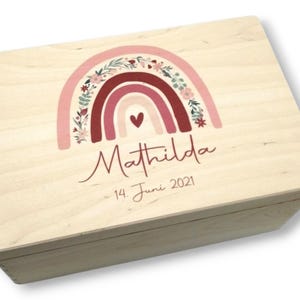 Könnte beinhalten: Eine Holzkiste mit einem rosafarbenen und roten Regenbogen-Design und floralen Akzenten. Die Kiste ist personalisiert mit dem Namen "Mathilda" und dem Datum "14. Juni 2021".