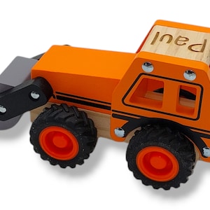 Könnte beinhalten: Ein orangefarbener Bulldozer aus Holz mit schwarzen Rädern und einer grauen Schaufel. Der Bulldozer hat eine Holzkabine mit dem Namen "Paul" darauf.
