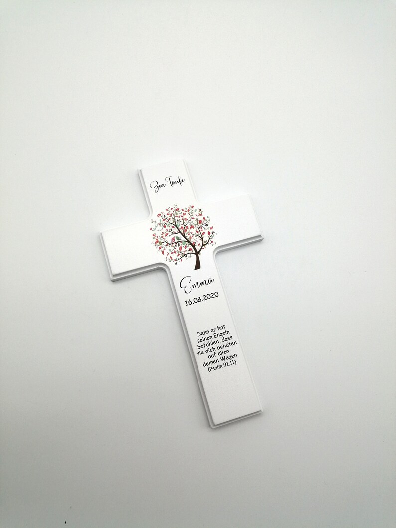 May include: White wooden cross with a pink and green tree design. The text "Zur Taufe" is at the top of the cross. The name "Emma" and the date "16.08.2020" are below the tree. The text "Denn er hat seinen Engeln befohlen, dass sie dich beh&uuml;ten auf allen deinen Wegen. (Psalm 91,11)" is at the bottom of the cross.