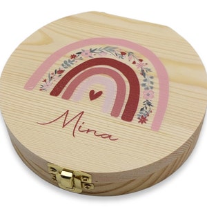 May include: A round wooden box with a hinged lid and a gold latch. The box is decorated with a pink, red, and white rainbow with floral accents and the name "Mina" written in cursive.