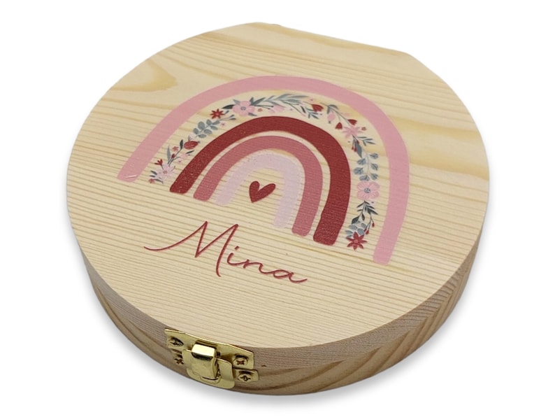 May include: A round wooden box with a hinged lid and a gold latch. The box is decorated with a pink, red, and white rainbow with floral accents and the name "Mina" written in cursive.
