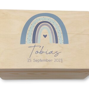 Könnte beinhalten: Eine Holzkiste mit einem hellblauen Regenbogen-Design und einem kleinen Herz in der Mitte. Die Kiste ist personalisiert mit dem Namen "Tobias" und dem Datum "15. September 2023".