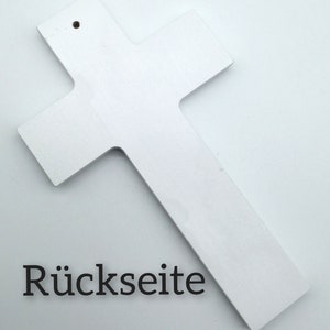 May include: White wooden cross with a hole at the top for hanging. The back of the cross is shown in the image. The text "R&uuml;ckseite" is printed on the bottom of the image.