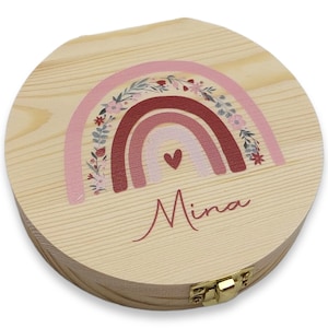 May include: A round wooden box with a hinged lid. The box is decorated with a pink and red rainbow with floral accents. The name "Mina" is written in cursive below the rainbow.