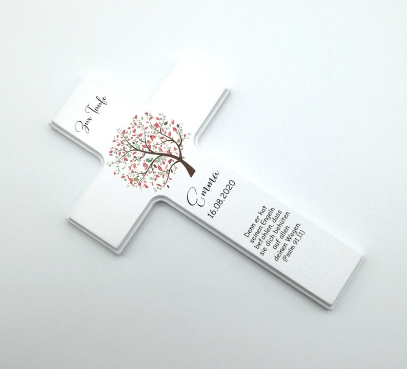 May include: White wooden cross with a pink and green tree design. The cross has the text "Zur Taufe Emma 16.08.2020" and a bible verse.