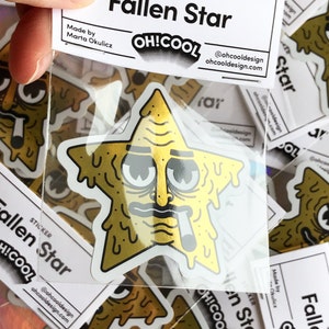 Op de afbeelding: Een gouden sticker met een cartoonster met een smeltend gezicht, een zonnebril en een sigaret. De sticker is gelabeld met "Fallen Star" en "OH!COOL" met het websiteadres "ohcooldesign.com".
