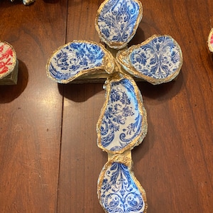 May include: A gold-painted cross made of five oyster shells. Each shell is decorated with a blue and white floral pattern.
