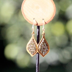 Peut inclure: Boucles d'oreilles pendantes en filigrane dorées en forme de larme. Les boucles d'oreilles sont présentées sur un support en bois.