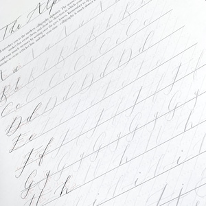 Puede incluir: Un primer plano de un cuaderno de papel rayado con letras manuscritas en cursiva del alfabeto, comenzando con la letra "A" y continuando hasta "H". Las letras est&aacute;n escritas en gris claro, con una l&iacute;nea gris m&aacute;s oscura debajo de cada letra.