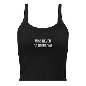 Peut inclure: Haut court noir avec de larges bretelles et le texte "MISS NEVER DO NO WRONG" en blanc. Le haut est de couleur noire unie et possède une encolure arrondie.