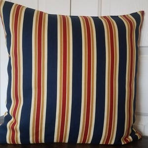 May include: A blue, red, and cream striped throw pillow with a square shape.