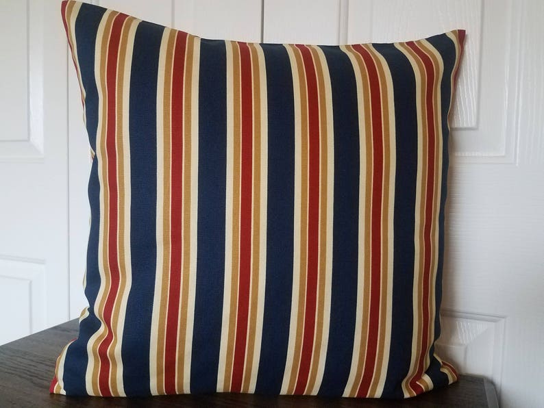 May include: A blue, red, and cream striped throw pillow with a square shape.