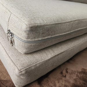 May include: Close-up of a beige sofa cushion with a zipper detail. The cushion is made of a soft, textured fabric.