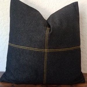 May include: Black denim pillow with yellow stitching in a cross pattern.