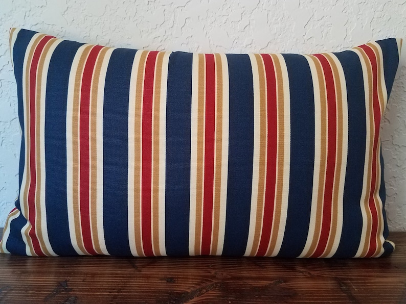 May include: A blue, red, and gold striped pillow with a rectangular shape. The pillow is made of a soft, woven fabric.