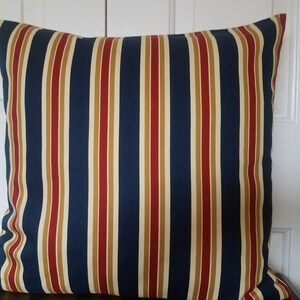 May include: A striped pillow with navy blue, red, and beige stripes. The pillow is made of a soft, woven fabric.