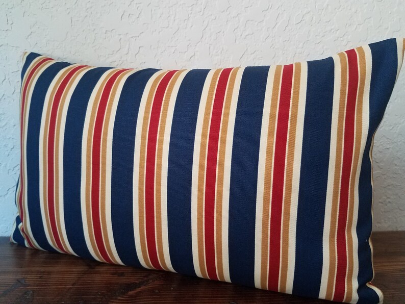 May include: A navy blue, red, and gold striped throw pillow. The pillow is rectangular and has a soft, plush feel.