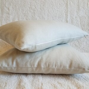 May include: Two light gray linen pillow covers stacked on top of each other. The pillow covers are made of a soft, natural fabric and have a subtle texture.