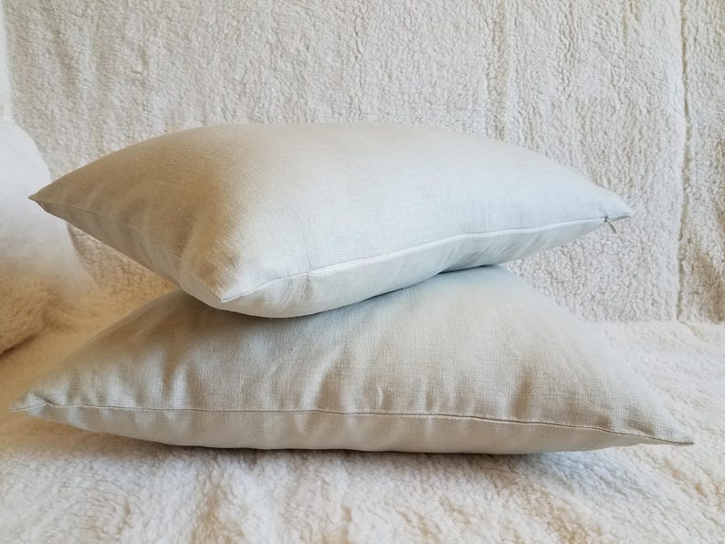May include: Two light gray linen pillow covers stacked on top of each other. The pillow covers are made of a soft, natural fabric and have a subtle texture.