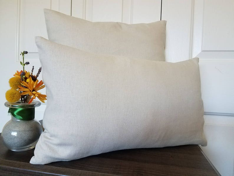 May include: Two beige linen pillow covers, one on top of the other. The pillow covers are made of a soft, natural fabric and have a simple, elegant design.