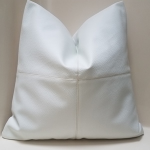 May include: A large, square white pillow with a textured surface. The pillow is divided into four sections by stitched seams, creating a subtle geometric pattern. The seams are a light beige color. The pillow is a decorative home accent.