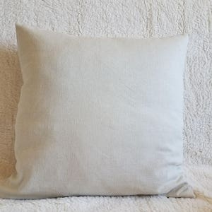 May include: A plain white pillow with a smooth, linen-like texture. The pillow is lying on a white fluffy surface.