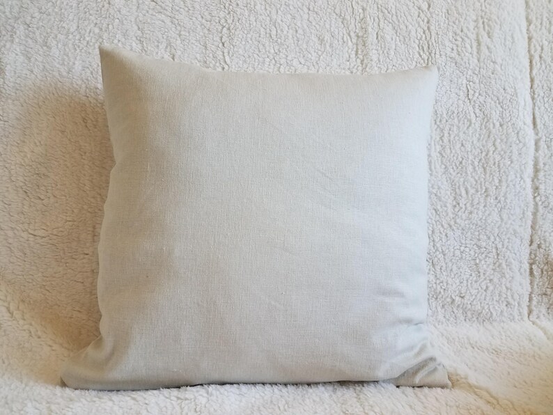 May include: A plain white pillow with a smooth, linen-like texture. The pillow is lying on a white fluffy surface.