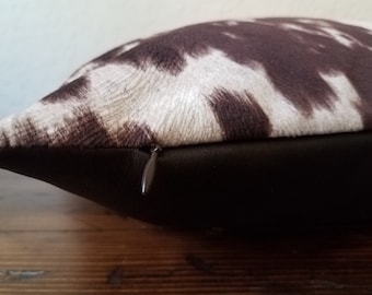 May include: A brown and white cowhide patterned throw pillow with a zipper closure.