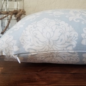 May include: A light blue throw pillow with a white damask pattern. The pillow has a zipper closure.