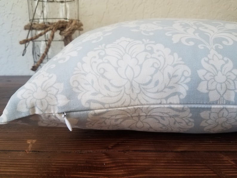 May include: A light blue throw pillow with a white damask pattern. The pillow has a zipper closure.
