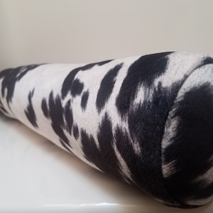 May include: A black and white cow print bolster pillow. The pillow is cylindrical and has a soft, plush texture.
