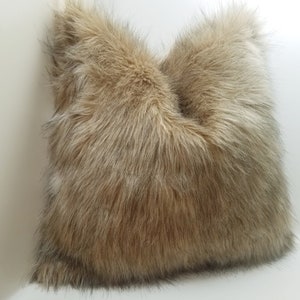 May include: A brown and beige faux fur throw pillow. The pillow is made of soft, plush fabric and has a fluffy texture.