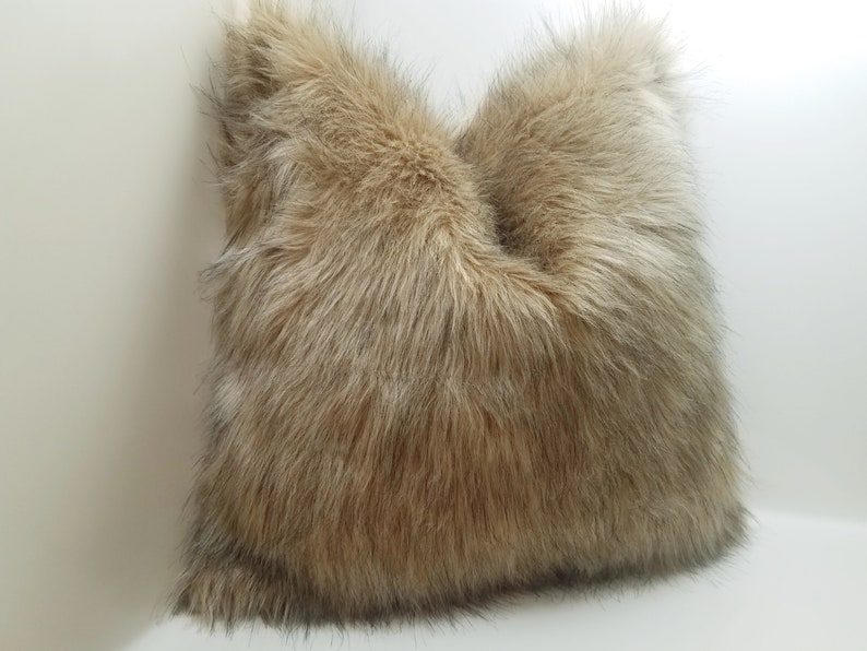 May include: A brown and beige faux fur throw pillow. The pillow is made of soft, plush fabric and has a fluffy texture.