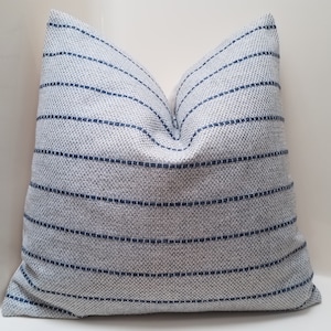 May include: A gray and blue striped throw pillow with a subtle texture. The pillow is made of a soft, woven fabric.