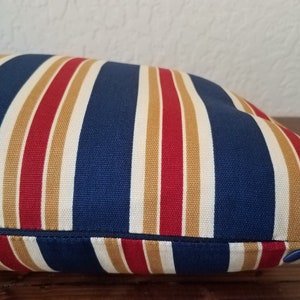 May include: A blue, red, and tan striped pillow with a zipper closure.