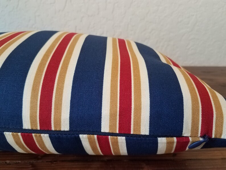 May include: A blue, red, and tan striped pillow with a zipper closure.
