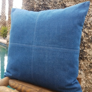 May include: A blue denim pillow with a decorative stitched design. The pillow is sitting on a wooden bench.