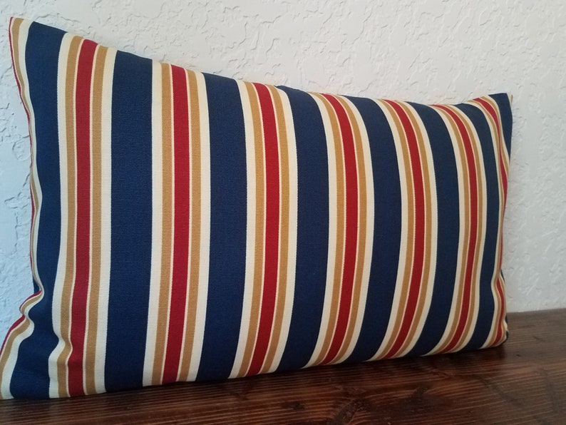 May include: A blue, red, and cream striped pillow cover. The pillow is rectangular and has a soft, textured fabric.