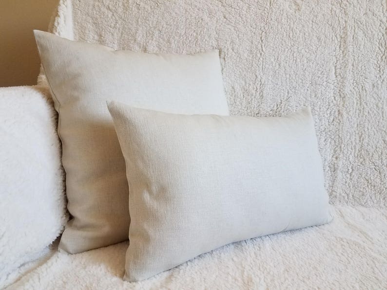 May include: Two off-white rectangular pillows on a white fluffy surface. The pillows are made of a soft, textured fabric.