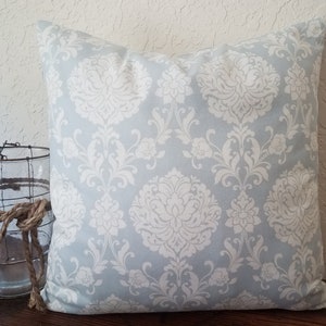 May include: A light blue throw pillow with a white damask pattern. The pillow is square and has a soft, plush feel.