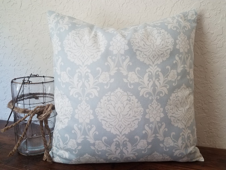 May include: A light blue throw pillow with a white damask pattern. The pillow is square and has a soft, plush feel.