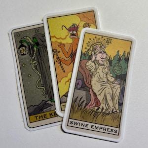 May include: Three tarot cards with illustrations of a green hooded figure with a snake, a red figure with a crown and an anchor, and a pink pig wearing a crown and a dress. The cards are labeled "The Key", "The Tower", and "Swine Empress".