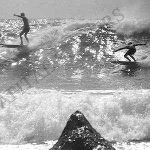 May include: Three surfers riding waves on a sunny day. The surfers are silhouetted against the bright sky and water. The waves are breaking and crashing around them.
