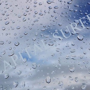 May include: A close-up of a window with raindrops on the glass. The word "CAPITAL SURFERS" is written on the glass in white lettering.