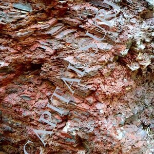 May include: Close-up of a layered rock formation with red, brown, and grey hues. The rock has a rough, textured surface.