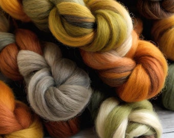 May include: A close-up of several skeins of yarn in various shades of brown, green, and yellow. The yarn is arranged in a pile, with the ends of the skeins visible.