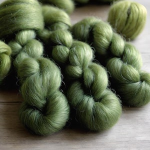 May include: A close-up of a bundle of soft, green yarn. The yarn is twisted and knotted, creating a textured and fluffy appearance.