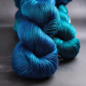 May include: A skein of teal blue and dark blue silk yarn. The yarn is soft and lustrous, and it is perfect for knitting or crocheting.