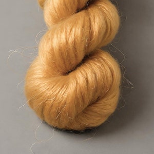 May include: A close-up of a skein of golden-yellow yarn. The yarn is tightly twisted, with a soft, fuzzy texture and visible strands. The yarn is a warm, inviting color, perfect for knitting or crocheting projects.