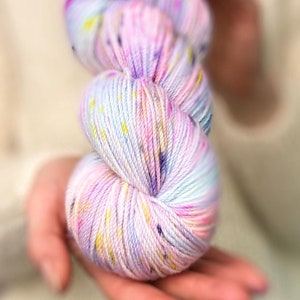 May include: A skein of colorful yarn with a white base and splashes of pink, purple, and yellow.